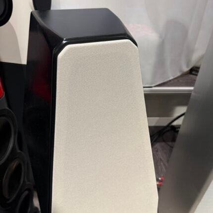 Close-up of a floor-standing speaker with a beige fabric grille and glossy black enclosure edge.