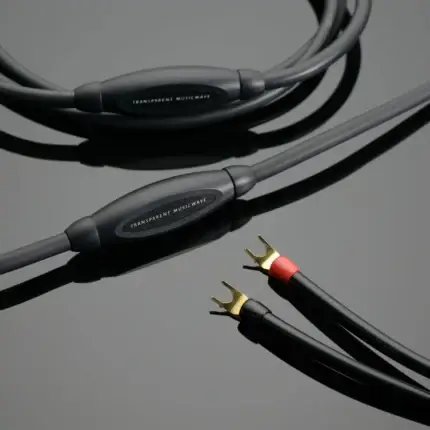 Close-up of black audio cables with gold-plated connectors on a gray surface; the label 'Transparent MusicWave' is visible on the housings.