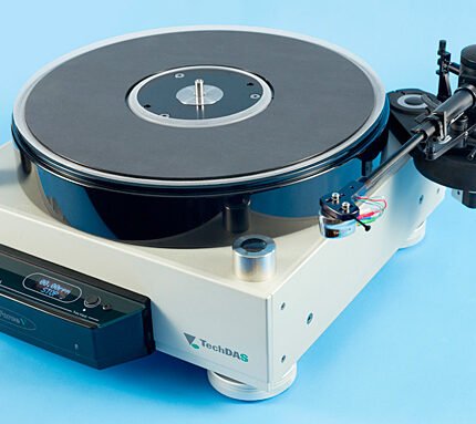 White TechDAS turntable with black platter and tonearm, plus a control box on the left, set on a blue background.