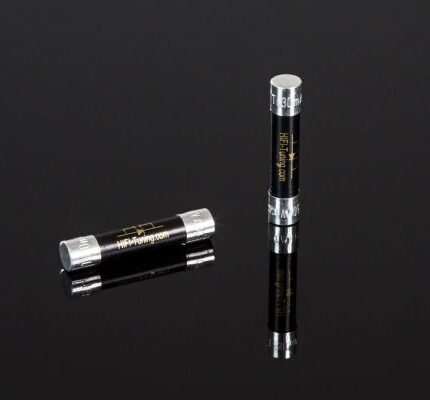 Two black and silver lip balm tubes on a reflective black surface, one standing upright and one lying down.