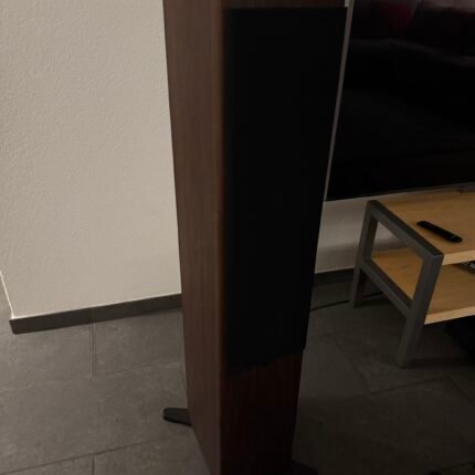 Close-up of a tall dark wooden furniture leg with a black side panel, next to a TV and a small wooden table with a remote on it in a living room.