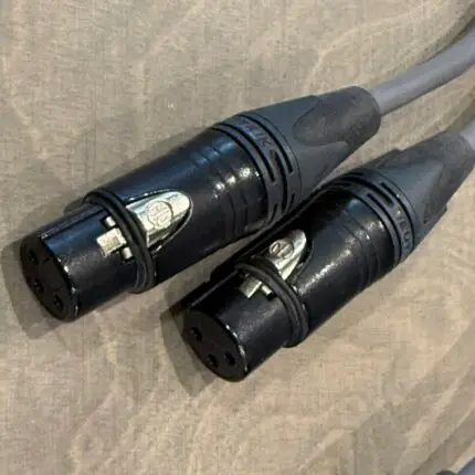 Two black circular XLR-style connectors connected to a gray cable, resting on a beige textured surface